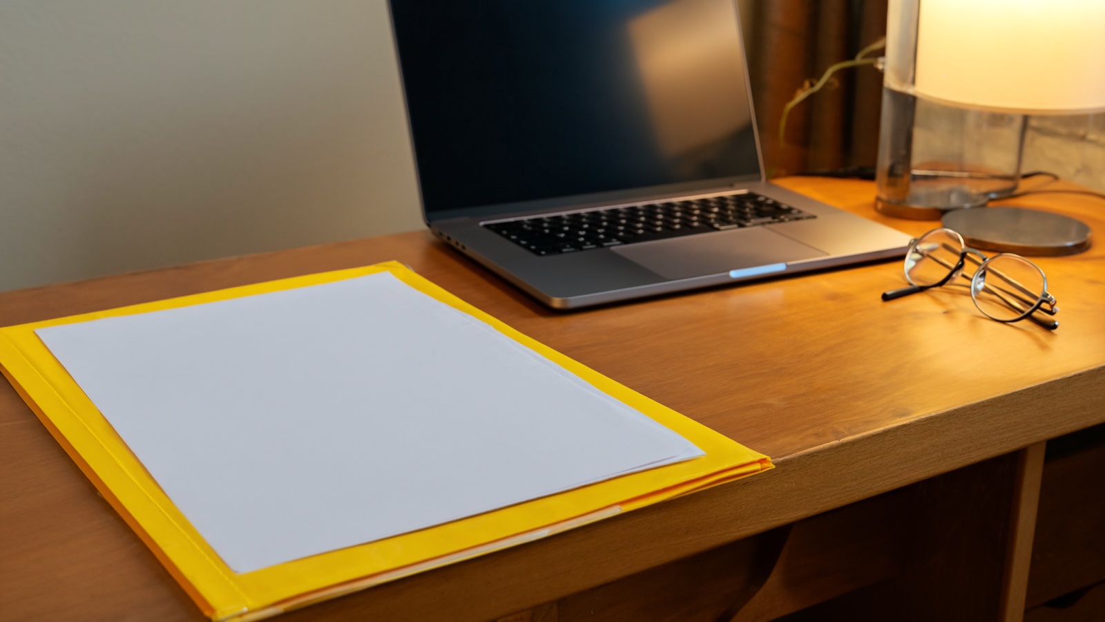Tidy home office desk with a folder of documents, laptop, and reading glasses